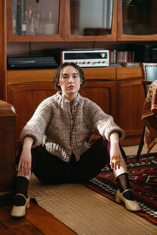 Woman sitting on a rug in a room with wooden furniture and a patterned rug.